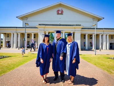 three graduates in front of de montfort hall