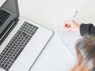 person looking at laptop writing with pen